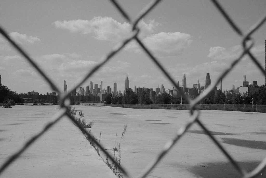 Monochrome industrial city beyond a chain-link fence